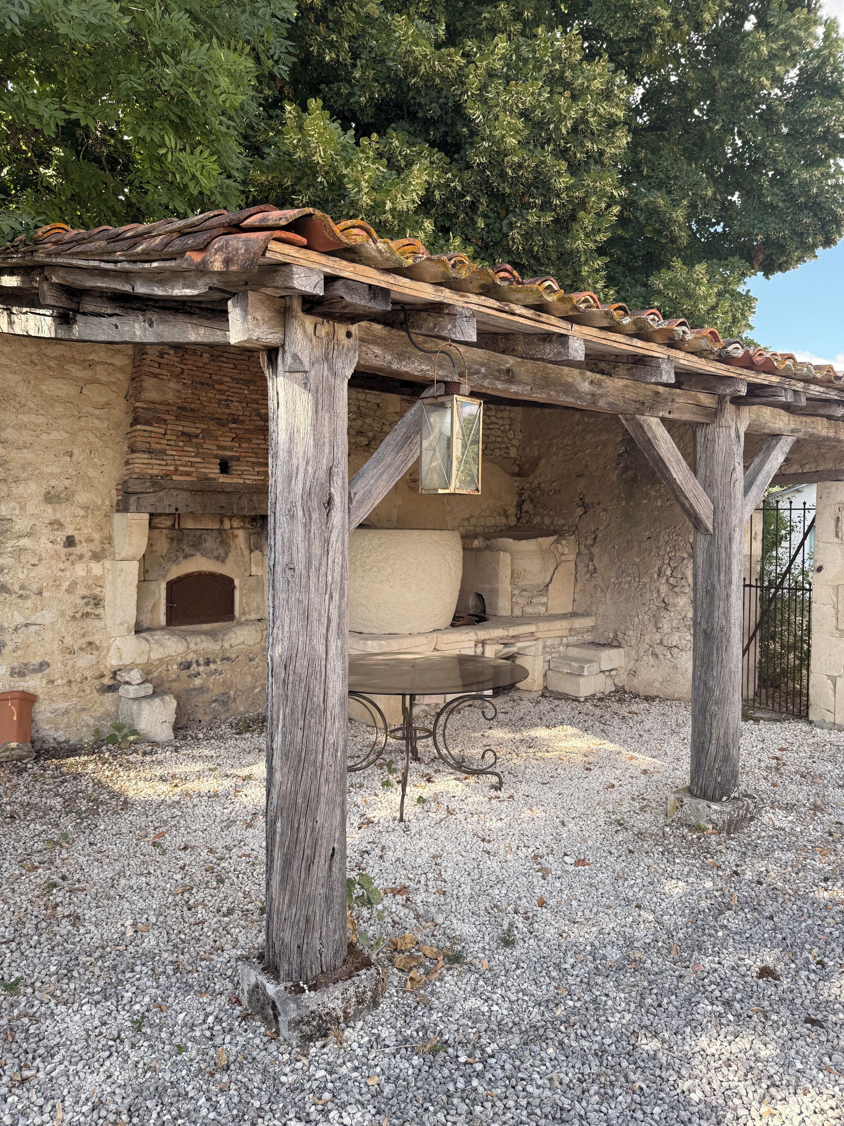 Un edificio de piedra con un porche de madera rústico, un banco de piedra y un horno de ladrillo.