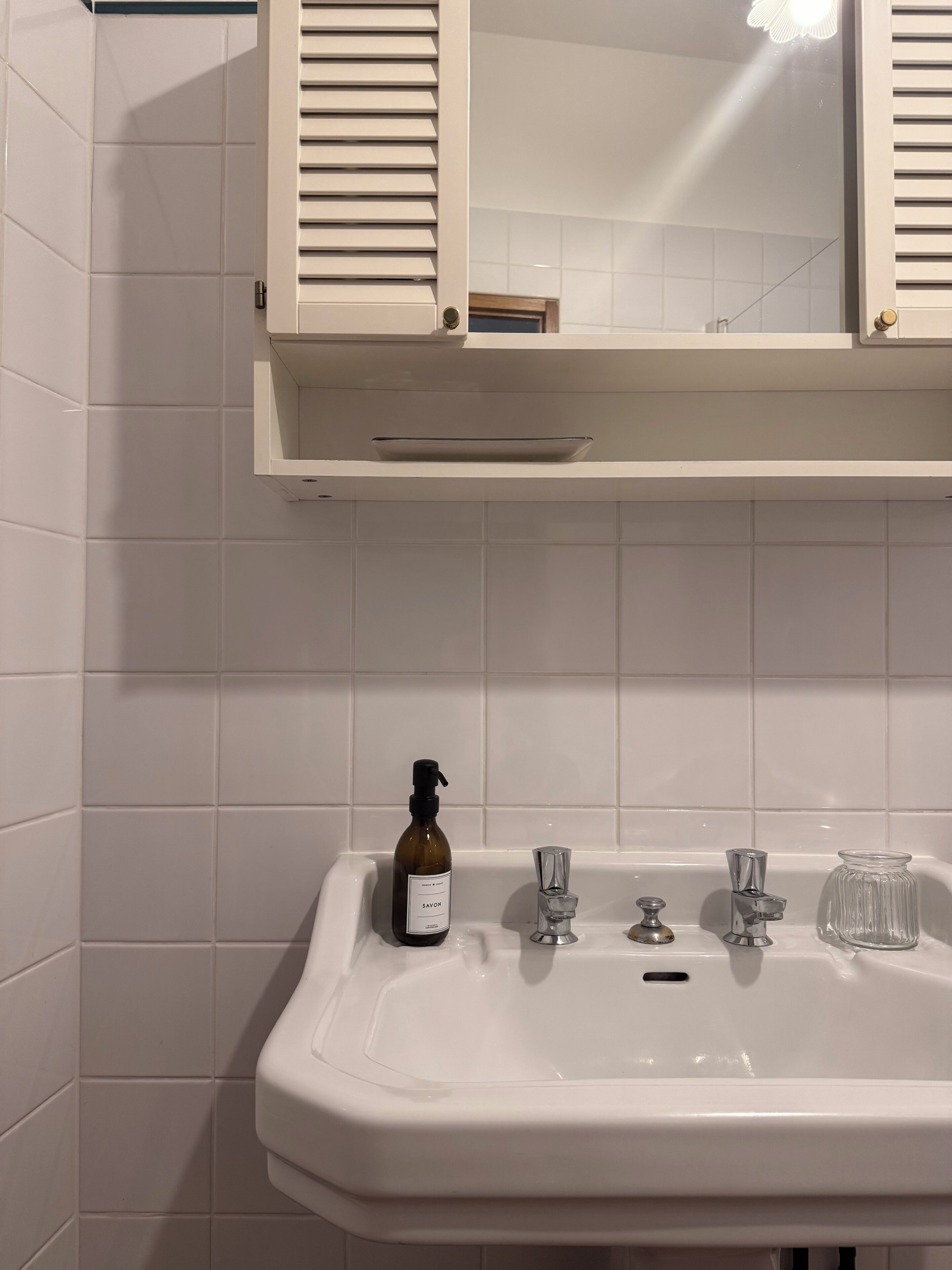 Un baño con lavamanos blanco, espejo y una botella de jabón.