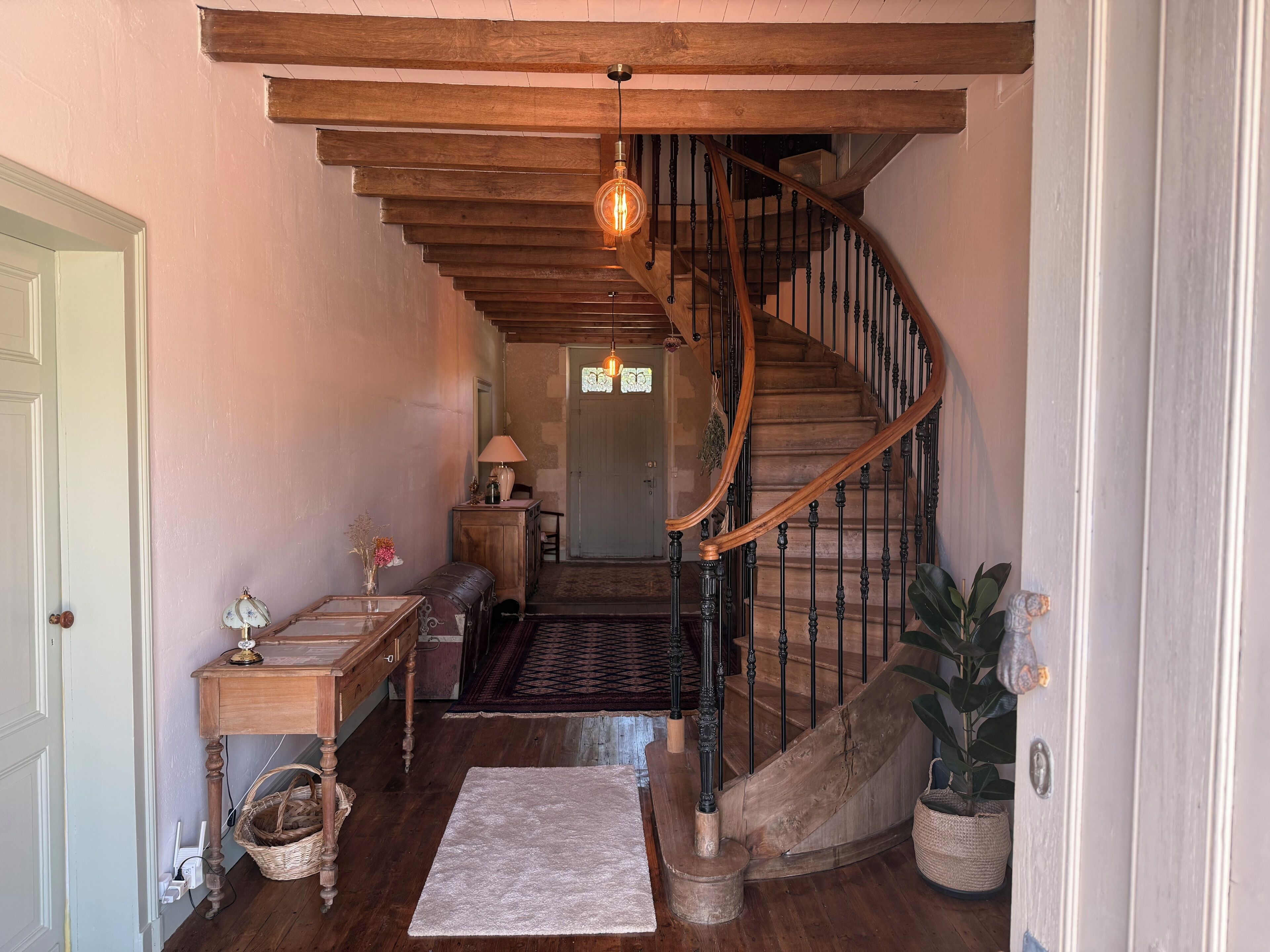 A wooden staircase with a wrought iron railing, a lamp, a small table with a vase, and a rug on the floor.