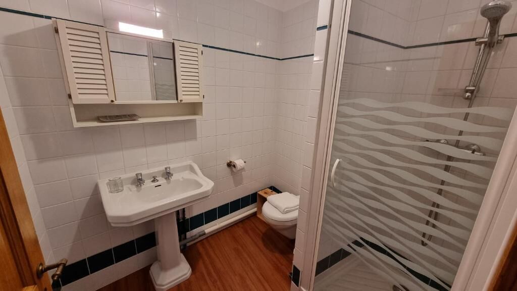 A bathroom with a pedestal sink, toilet, and a glass-enclosed shower area.