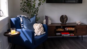 Un saló amb un sofà blau, una taula petita amb un got d'aigua, una planta i un televisor fixat a la paret.