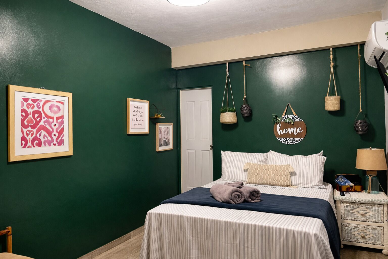 Ett sovrum med en säng, ett sängbord, en lampa och dekorationer på väggarna, inklusive inramade bilder och en skylt.