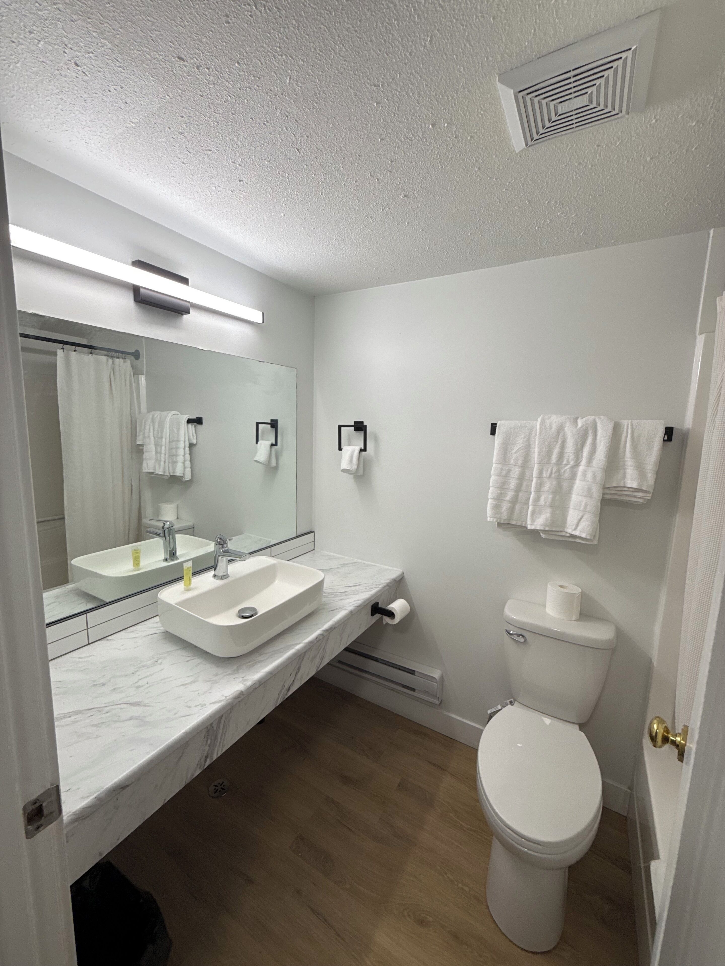 A bathroom with a white sink, mirror, and toilet, marble countertop, and wooden flooring.