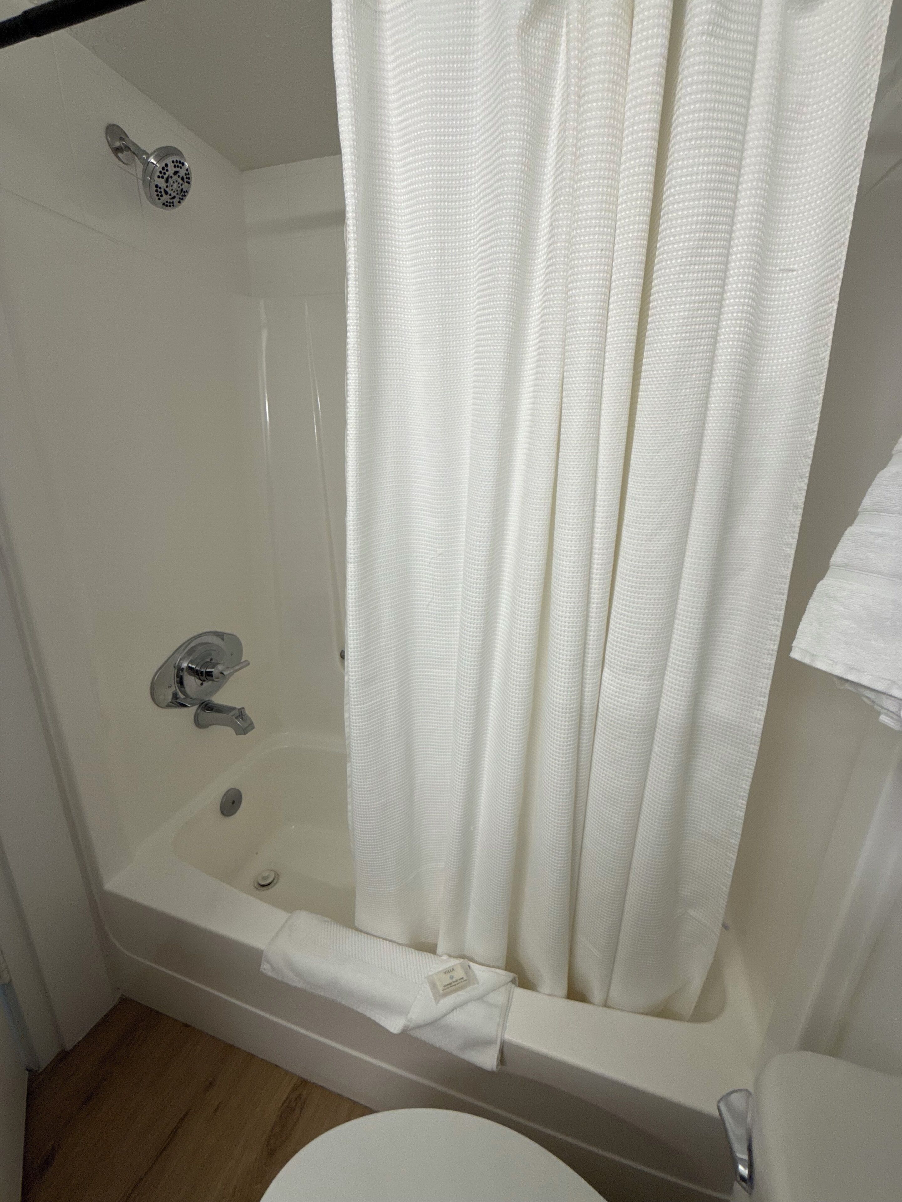 Una bañera blanca con ducha, una toalla y un inodoro a la vista.