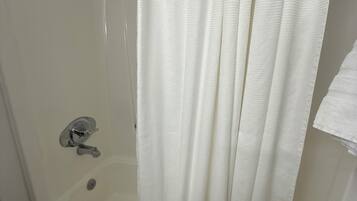 Una bañera blanca con ducha, una toalla y un inodoro a la vista.