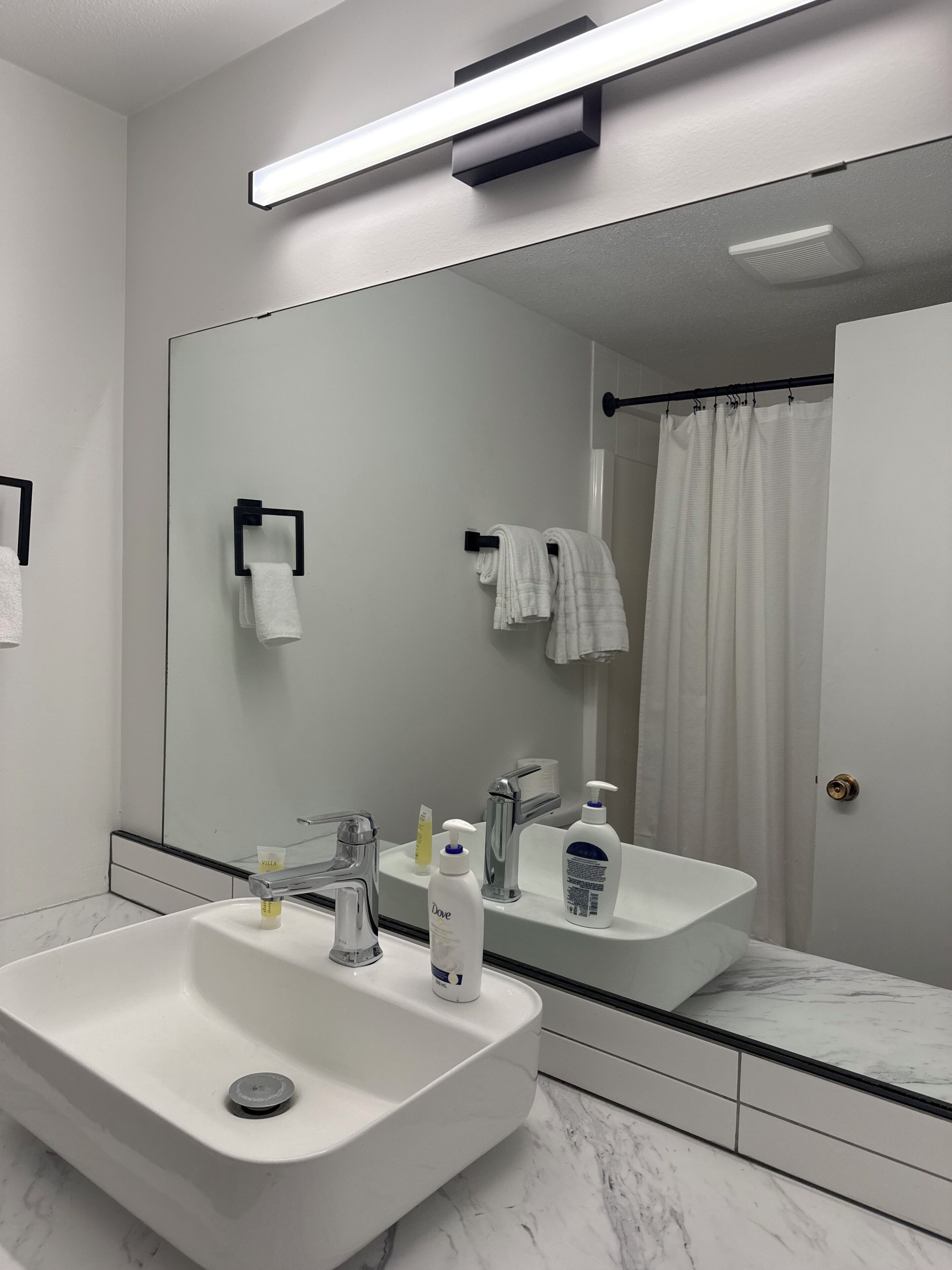 A modern bathroom with a large mirror, two sinks, a shower curtain, and toiletries.
