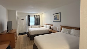 Hotellihuone, jossa on kaksi sänkyä, työpöytä, televisio ja ovi, joka johtaa toiseen huoneeseen.