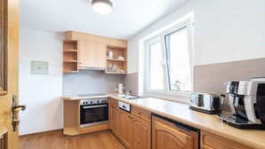A compact kitchen with wooden cabinets, a built-in oven, a dishwasher, a toaster, and a coffee maker. - Holiday Apartment in St. Anton (Sankt Anton am Arlberg)
