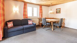 A cozy room with a sofa, a dining table, chairs, a radiator, and a window with curtains. - Holiday Apartment in St. Anton (Sankt Anton am Arlberg)