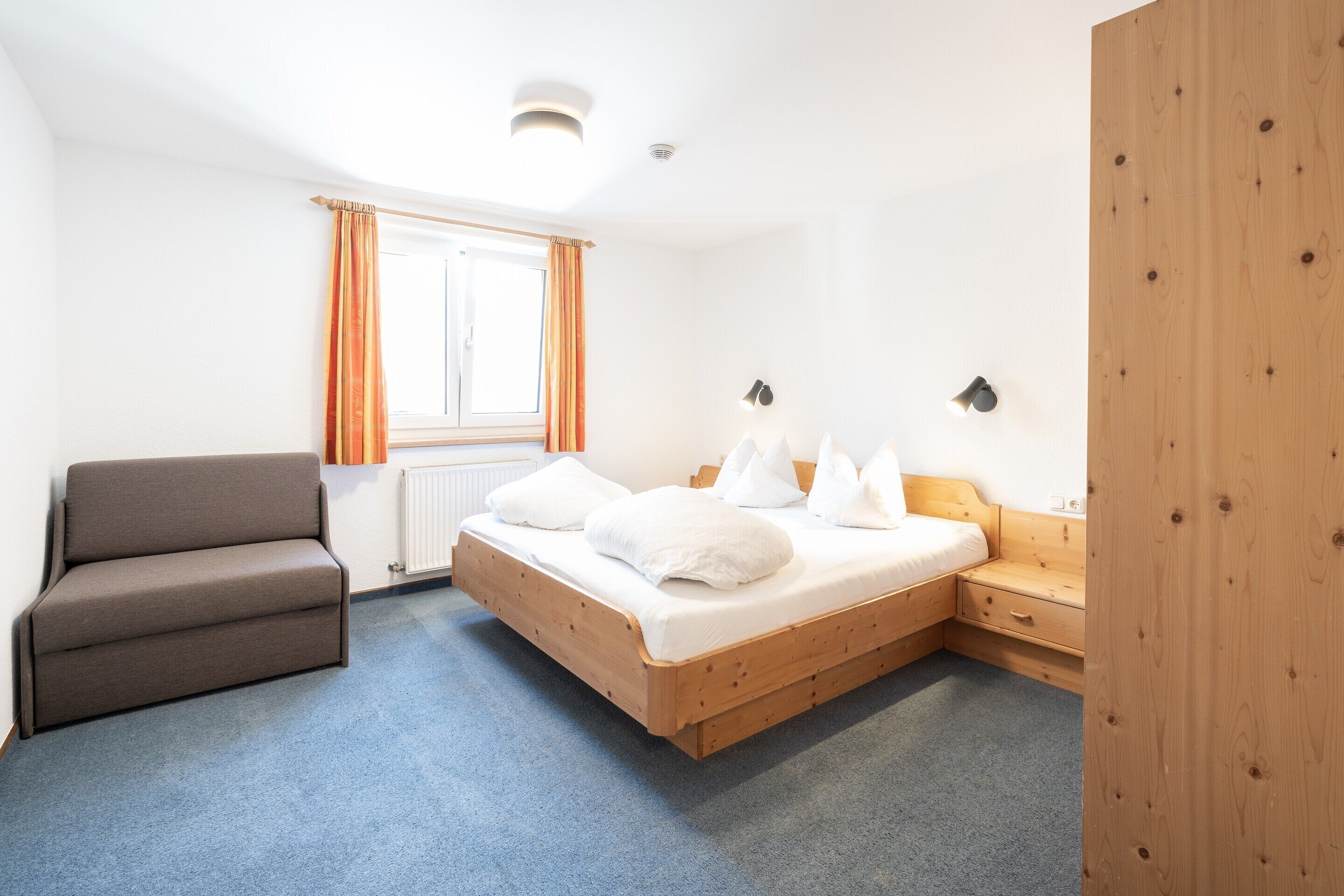 Une chambre à coucher comprenant un lit, un canapé, une table de chevet, une armoire en bois et une fenêtre avec des rideaux.