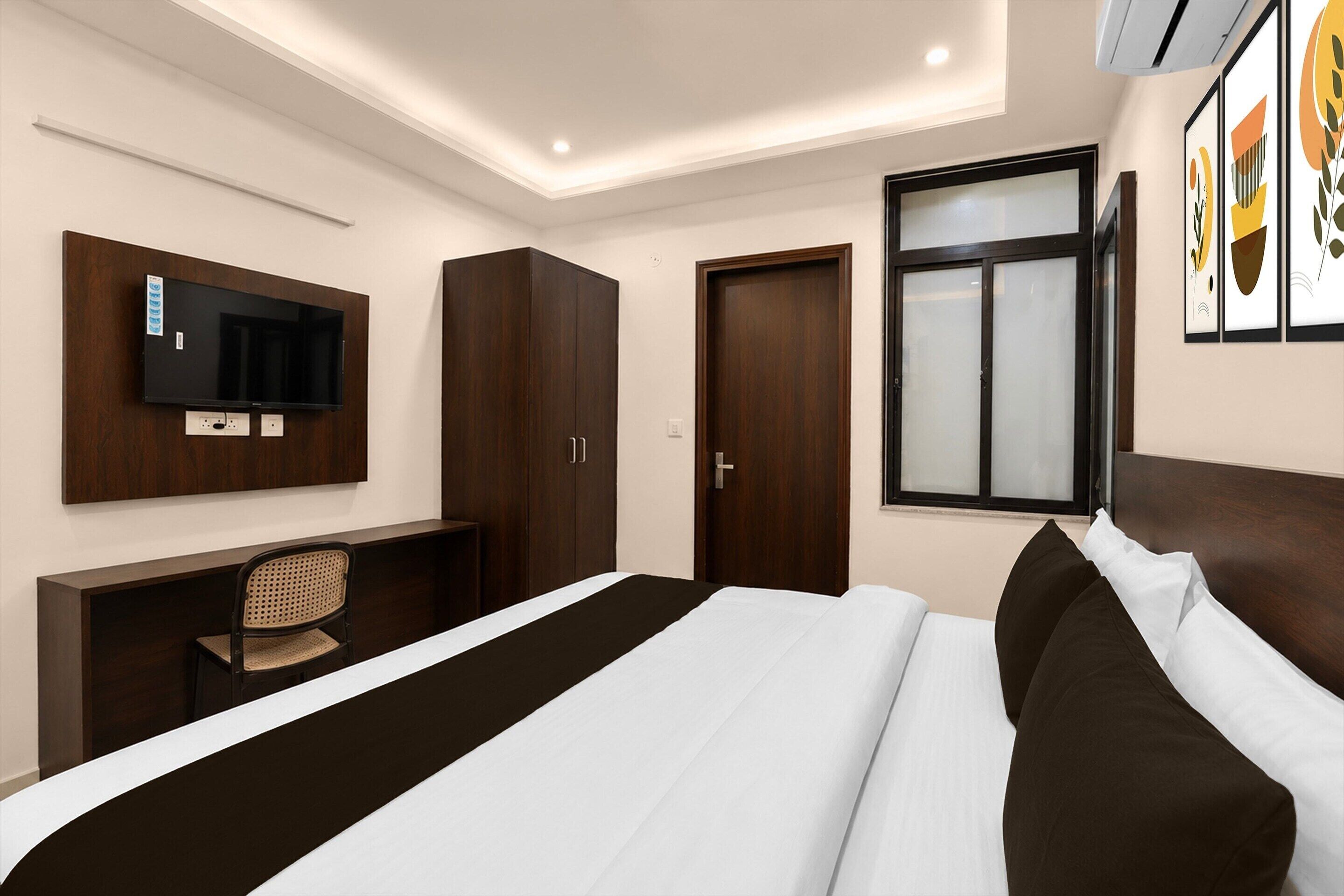 A hotel room with a bed, a desk with a chair, a wardrobe, a television mounted on the wall, and a window.
