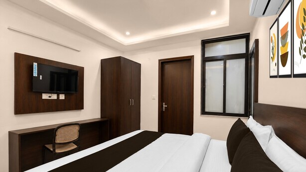 A hotel room with a bed, a desk with a chair, a wardrobe, a television mounted on the wall, and a window. - Deluxe Room Sanganer Court (Jaipur)