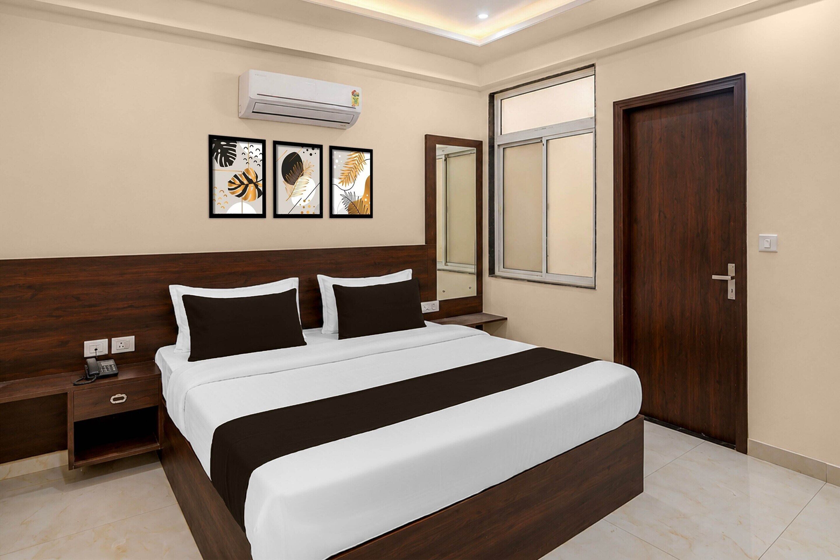 A hotel room with a large bed, a bedside table, a nightstand, an air conditioning unit, a window, and a door.