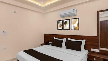 A hotel room with a bed, bedside tables, an air conditioning unit, and wall-mounted artwork.