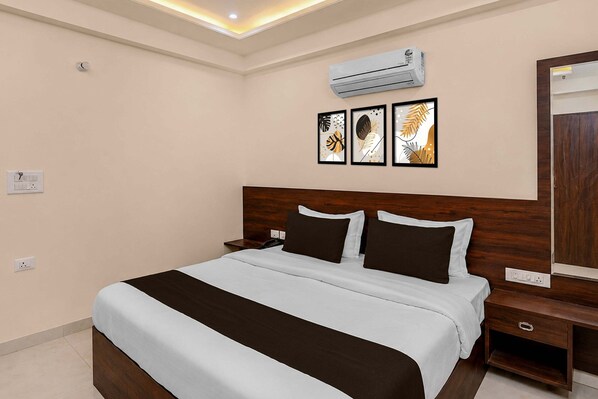 A hotel room with a bed, bedside tables, an air conditioning unit, and wall-mounted artwork.