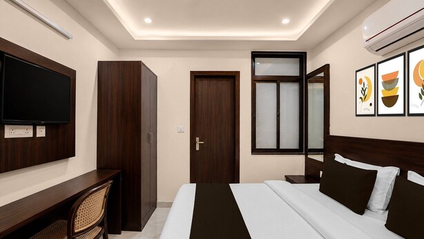 A hotel room with a bed, a desk, a chair, a television, a wardrobe, a door, a window, and wall art.