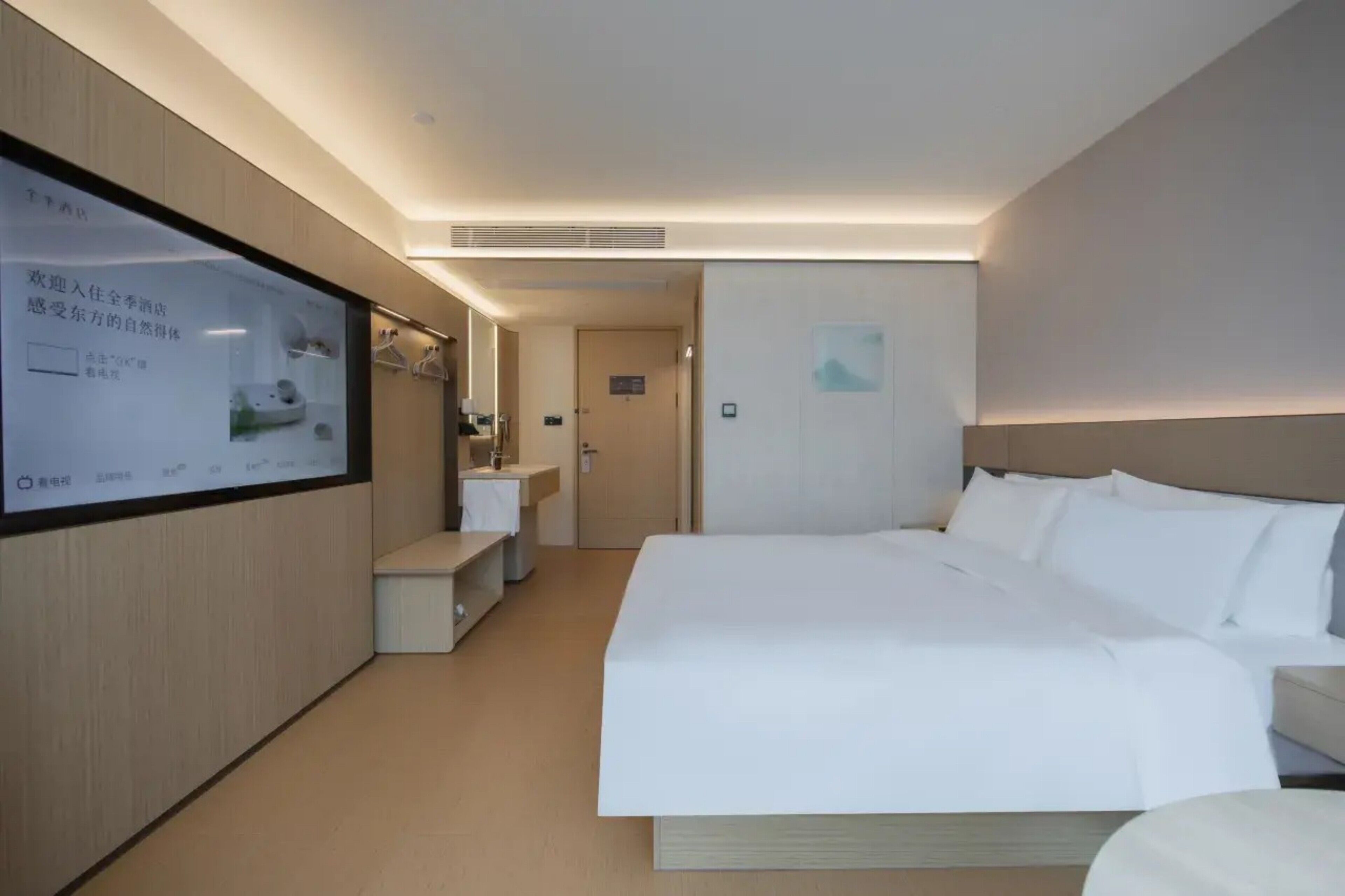 Una camera d'albergo con un letto, una televisione a parete, una piccola scrivania e una porta che dà su un'altra stanza.