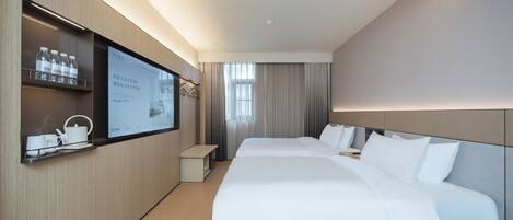 A hotel room with a large bed, a bedside table, a TV mounted on the wall, and a shelf with water bottles and a tea set.
