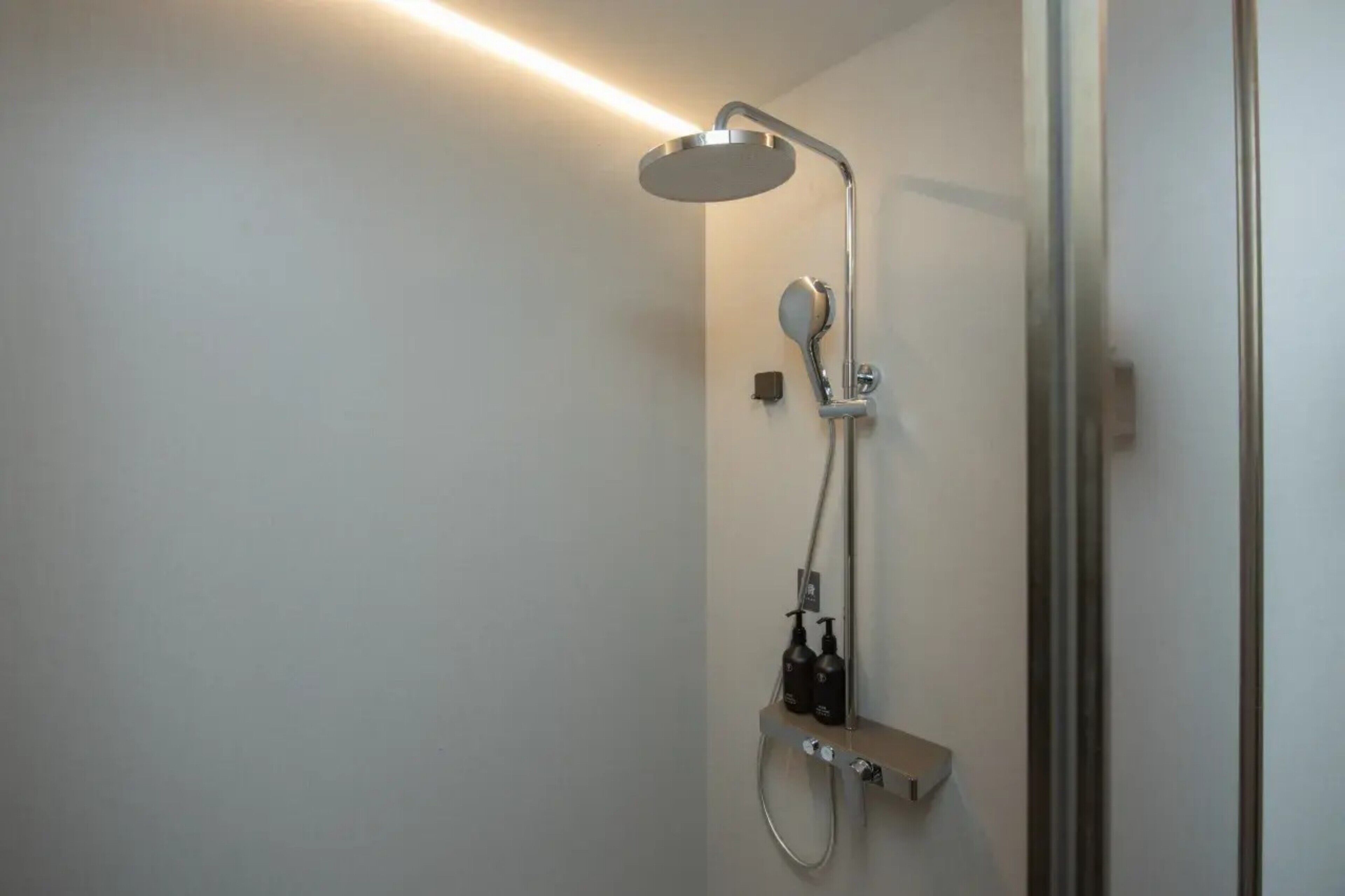Een moderne douche met een handdouche, een bediening aan de muur en een extra douchekop.
