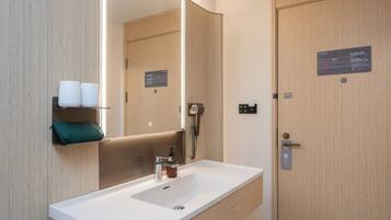 Un bagno moderno con uno specchio grande, un lavandino, un distributore di asciugamani e una porta con un cartello.
