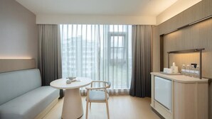 A modern hotel room with a sofa, a round table, a chair, a minibar, and large windows with curtains. - JI Hotel Fuzhou Railway Station  (Fuzhou)