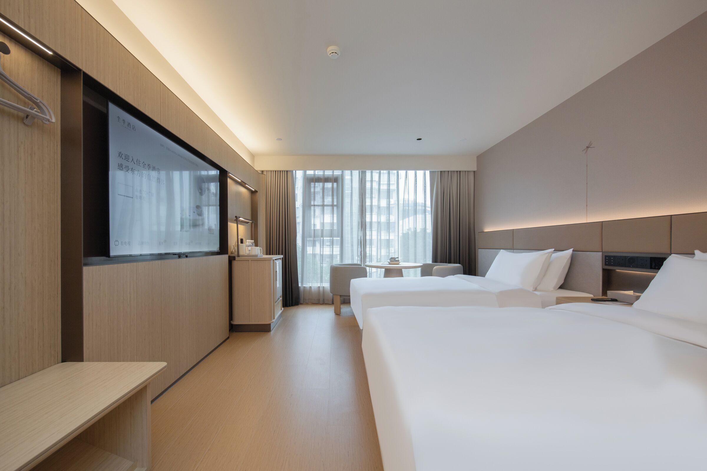 A hotel room with a large bed, a desk, a chair, a small table, and a TV screen.