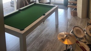 Et billardbord i et rum med et trommesæt, en stol og en hængende lampe.