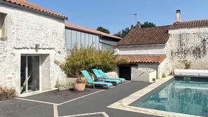 En gårdsplads med pool, stenvægge og blå liggestole.