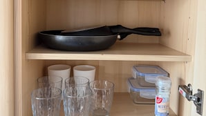 A kitchen cabinet with shelves holding cookware, glasses, and a container.