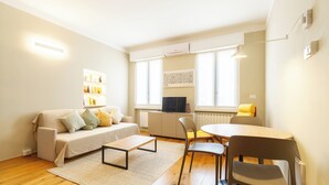 Una sala de estar moderna con sofá, mesa de centro, mesa de comedor, sillas y televisor.