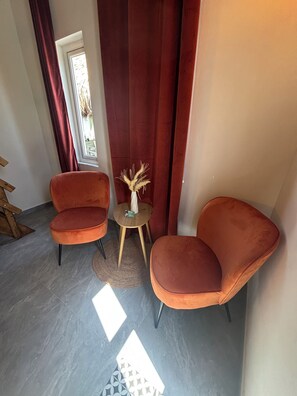 A room with two orange chairs, a small round table with a vase, and a window with curtains.