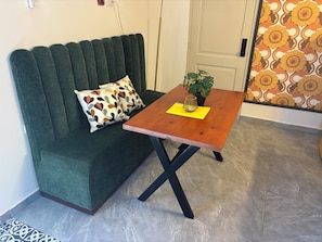 Ein grünes Sofa mit gemusterten Kissen, ein Holztisch mit gelbem Untersetzer und ein Blumentopf.