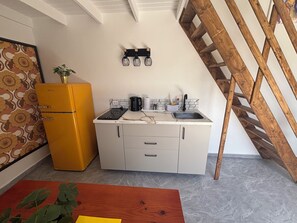 Eine kleine Küche mit einem gelben Kühlschrank, weißen Schränken und einer Holztreppe.