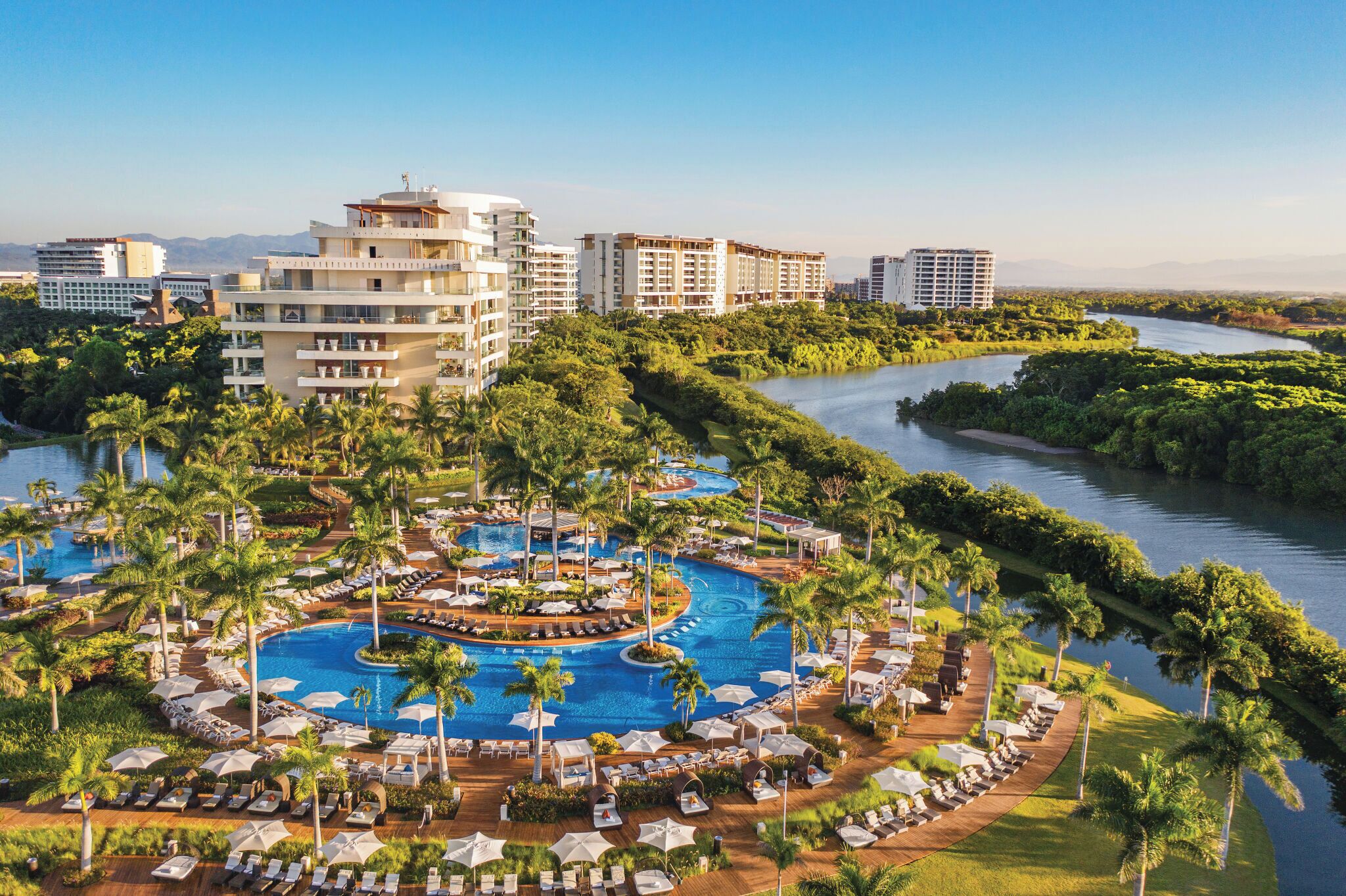 A resort with a central swimming pool, palm trees, and a river.