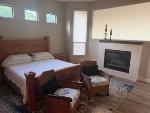 Ein Schlafzimmer mit einem großen Bett, zwei Korbstühlen, einem Kamin und drei Fenstern.