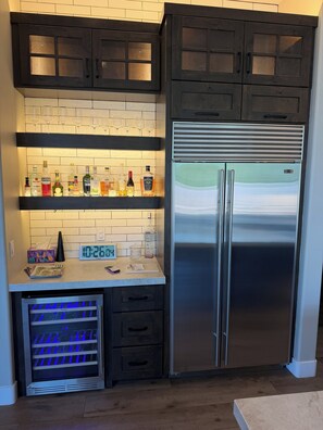 A kitchen with dark wooden cabinets, a stainless steel refrigerator, and a wine rack with glasses. - The Home is located in Troon north
Pool spa bbq island kitchen single level home (Scottsdale)