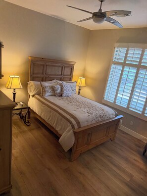 A bedroom with a wooden bed, two bedside lamps, a ceiling fan, and a window with blinds. - The Home is located in Troon north
Pool spa bbq island kitchen single level home (Scottsdale)
