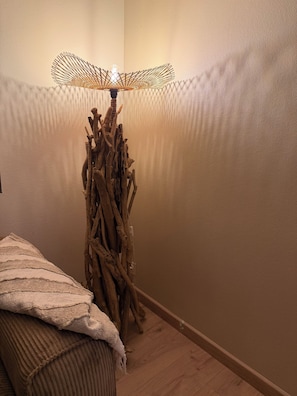 Ein Zimmer mit Holzboden, einem Bett mit gestreifter Decke und einer einzigartigen Lampe mit gewebtem Lampenschirm und Glühbirne.