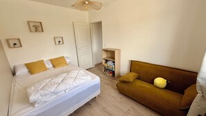 A bedroom with a bed, a sofa, a hanging light fixture, and a door. - La'PaillotteduBassin Vacation Rental (Le Teich)