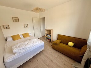 Ein Schlafzimmer mit einem Bett, einem Schlafsofa, einer Hängelampe und einer Tür.