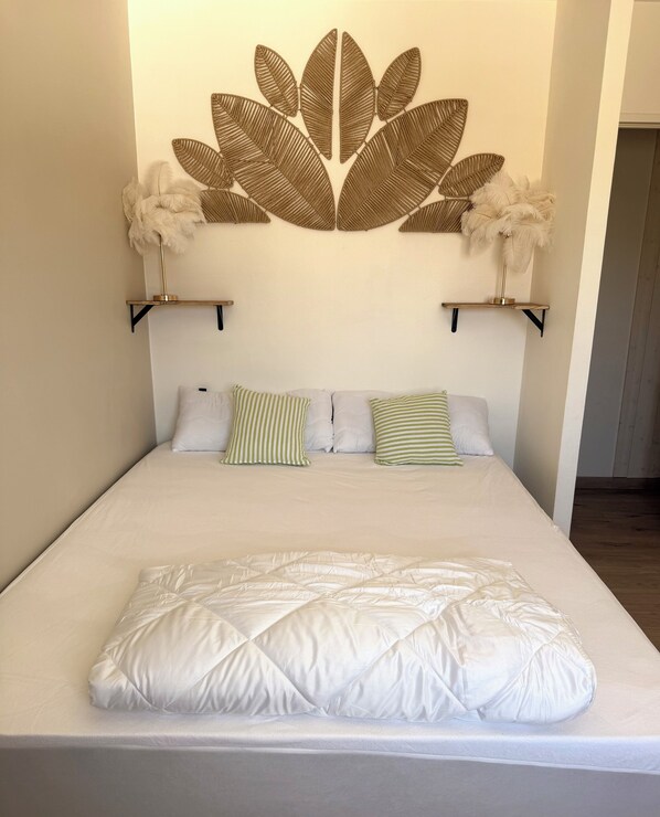Un lit avec une literie blanche, deux oreillers à rayures vertes et un élément décoratif mural au-dessus.