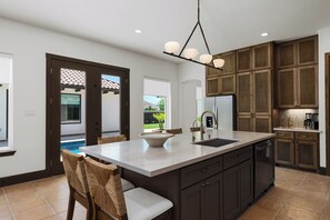 A modern kitchen with a large island, dark wooden cabinets, and a view to the outside. - La Perla Pool Home with Office (Port Isabel)