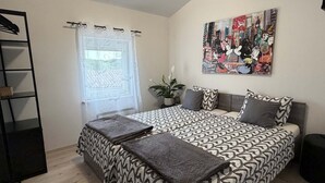 Une chambre avec une couvre-lit à motifs, une plante en pot, un tableau accroché au mur et une étagère noire.
