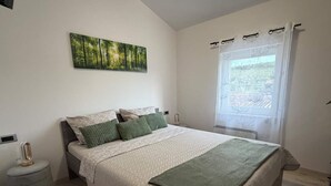 Une chambre à coucher comprenant un lit, une table de chevet, une commode, une fenêtre avec des rideaux et un tableau accroché au mur.
