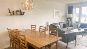 Una sala de estar moderna con una mesa de comedor de madera, un sofá gris y una araña.