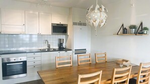 Una cocina moderna con armarios blancos, horno empotrado, cafetera y un comedor con mesa y sillas de madera.