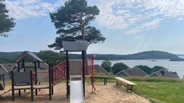A playground with a slide, climbing structures, and a view of a lake and hills. - 5 Star Holiday Home in Uddevalla (Uddevalla)