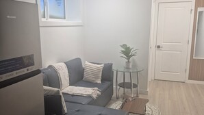 A compact living space with a sofa, ottoman, small table, and a potted plant. - Home  away from home, clean,  cozy and comfortable (Saskatoon)