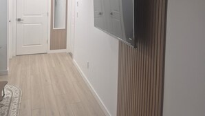 A hallway with a wooden floor, a white door, a mirror, and a wall-mounted TV. - Home  away from home, clean,  cozy and comfortable (Saskatoon)