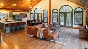 Un vaste espace de vie doté d’un plafond en bois, d’un grand canapé, d’une table basse et d’un coin repas avec des chaises et un bar.